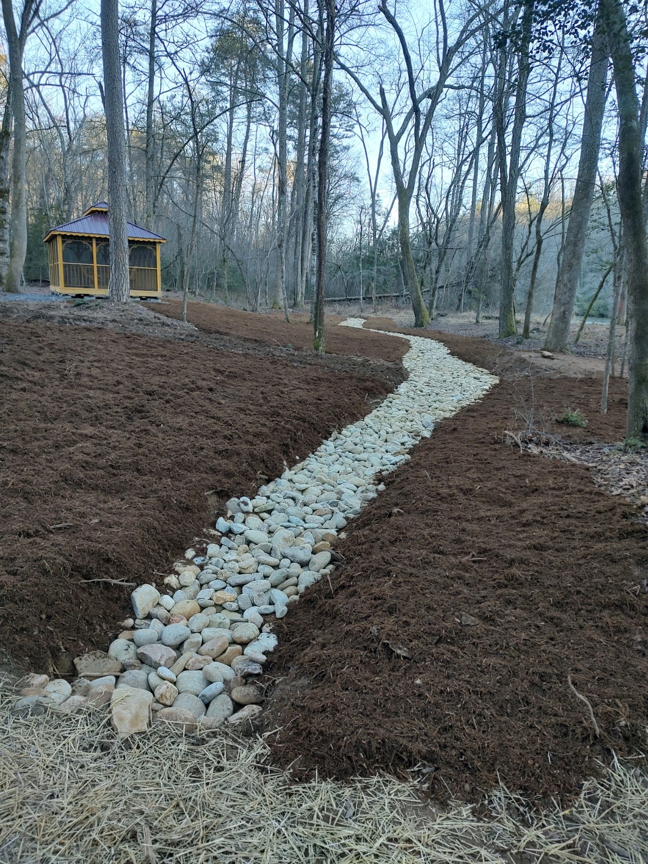 Gravel pathway through bare forest with gazebo
